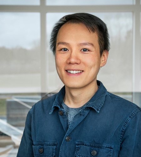 Picture of John Ruan in front of a set of windows with
				    the shade partially closed